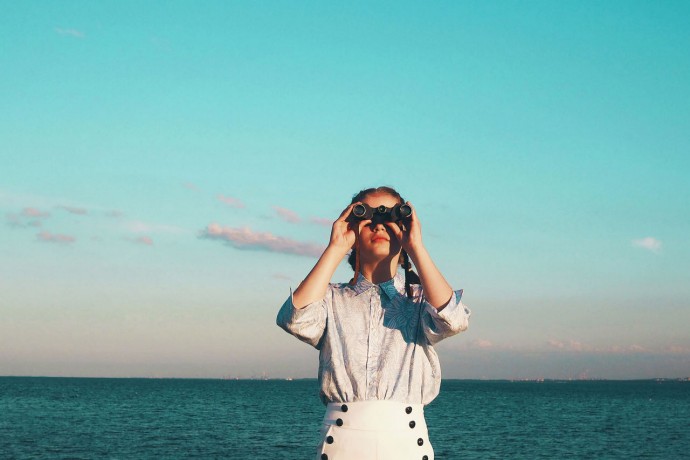 Young woman standing against sea and sky with binoculars